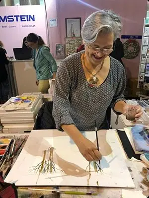 Ein Portrait der Künstlerin Sabine Dreher, die gerade mit einem Pinsel einen Baum auf ein Papier malt.