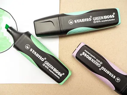 Drei Öko-Textmarker von STABILO liegen auf einem grauen Untergrund. Der grüne Textmarker ist geöffnet. Foto: Johanna Rundel