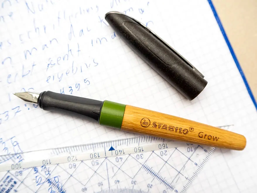 Ein klimaneutraler Füllfederhalter mit Holzschaft von STABILO liegt geöffnet, zusammen mit einem Geodreieck, auf einem Rechenheft. Foto: Johanna Rundel