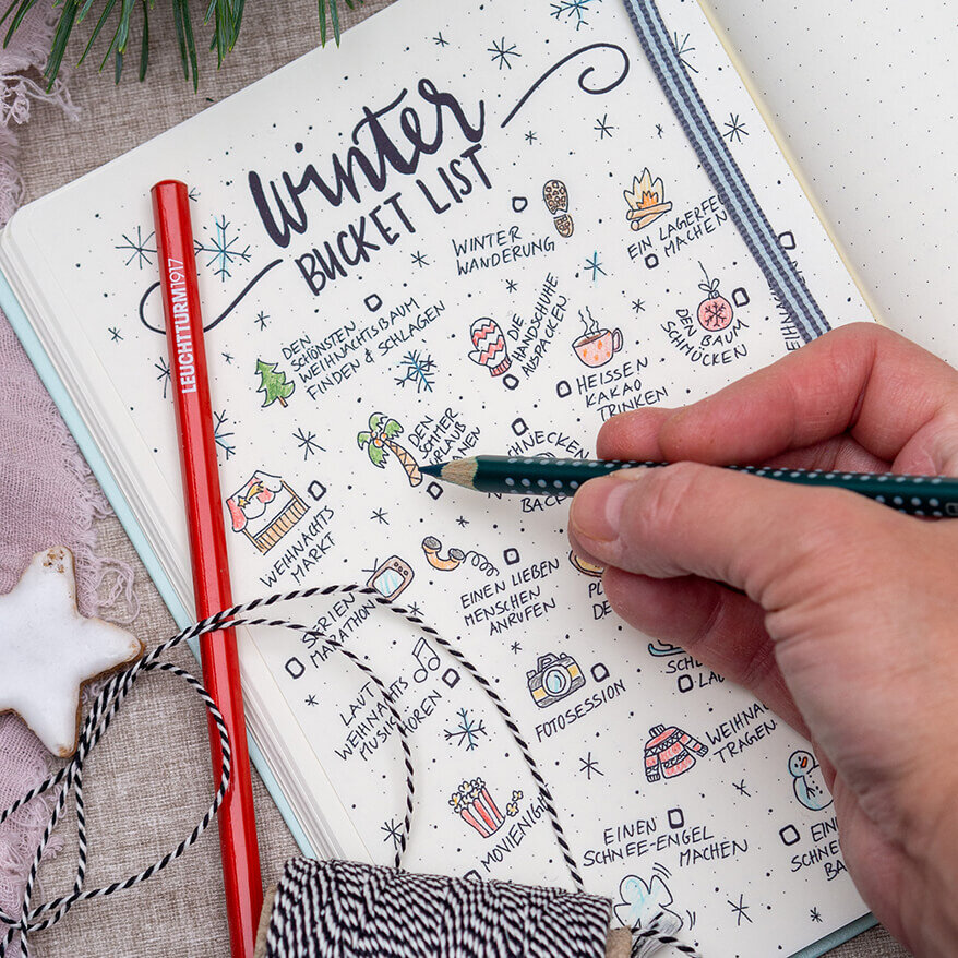 Jemand malt mit Buntstiften kleine Doodle-Zeichnungen einer Winter-Bucket-Liste in einem Notizbuch von LEUCHTTURM1917 farbig aus. Foto: Johanna Rundel