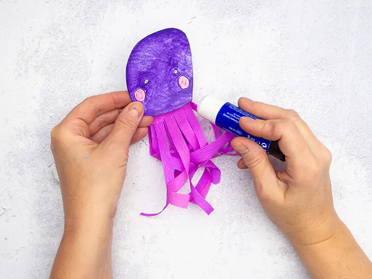 Jemand klebt mit einem Klebestift lila Krepppapierstreifen an einen Quallenkopf aus Papier. Foto: Johanna Rundel