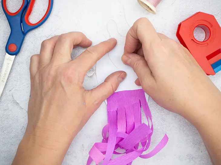 Jemand klebt einen Faden mit Klebefilm auf die Rückseite einer Qualle aus Papier. Foto: Johanna Rundel