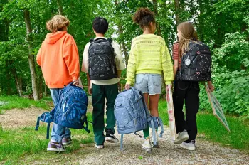 Eine Gruppe Jugendliche laufen mit Ihren Schulrucksäcken von coocazoo durch einen grünen Wald.