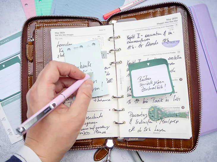 Jemand trägt mit einem rosa Kugelschreiber Termine in einen dunkelbraunen Planer von Filofax ein. Foto: Johanna Rundel