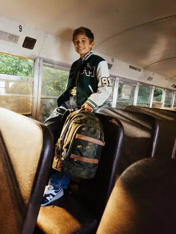 Ein Schüler steht mit seinem Schulrucksack von satch in der Hand im Gang eines Schulbusses.