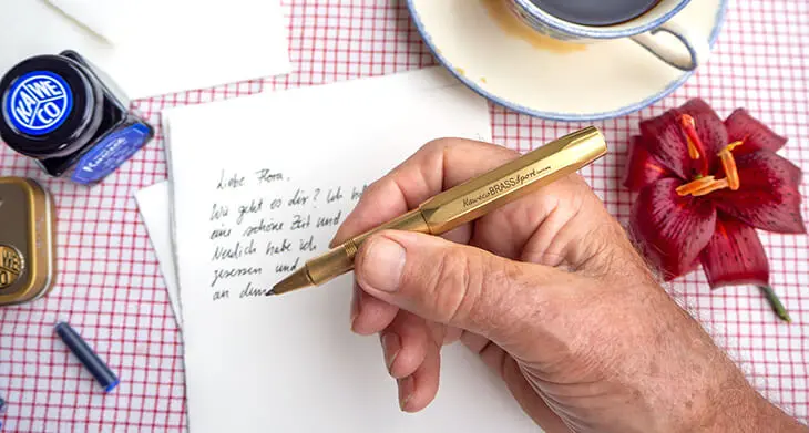 Die Hand eines älteren Herren schreibt mit einem goldenen Kugelschreiber von Kaweco einen Brief an sein Enkelkind. Foto: Johanna Rundel