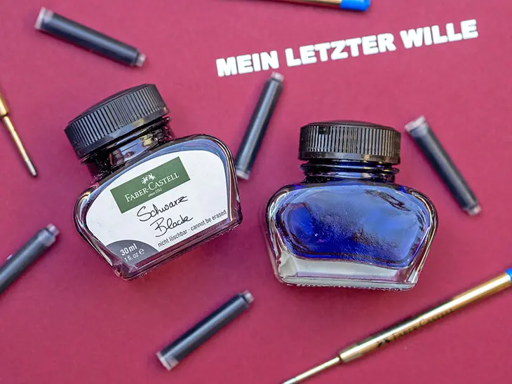 Auf einer roten Dokumentenmappe mit der Aufschrift „Mein letzter Wille“ liegen zwei Tintenfässer sowie zahlreiche Tintenpatronen von Faber-Castell. Foto: Johanna Rundel