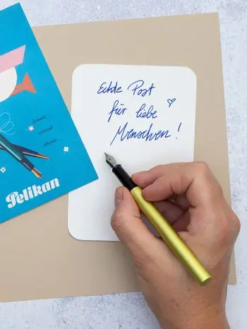 Jemand schreibt mit einem grünen Ineo-Füller von Pelikan einen Gruß auf die Rückseite einer Postkarte. Foto: Johanna Rundel