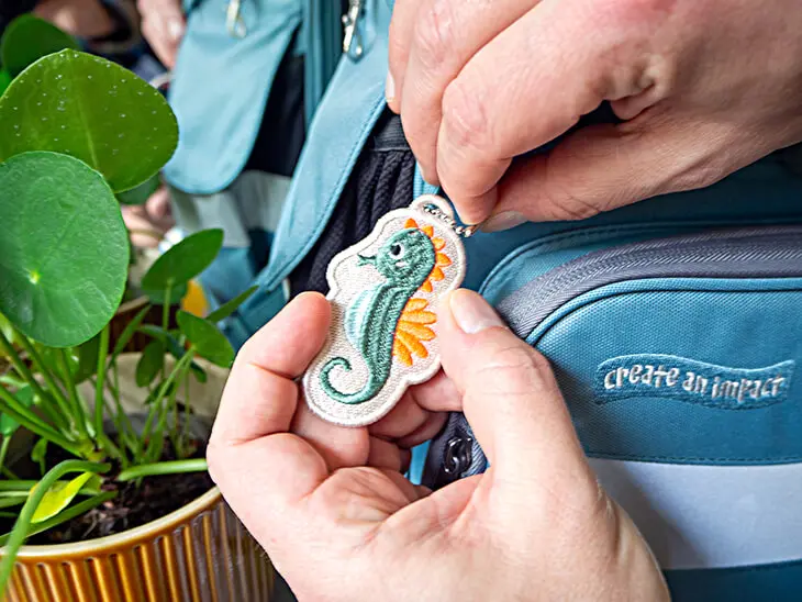 Jemand entfernt einen Seepferdchen-Anhänger von einem blauen Schulranze von School Mood. Foto: Johanna Rundel