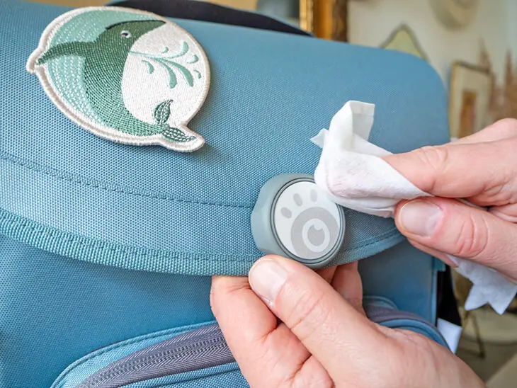 Jemand wischt mit einem Feuchttuch den Verschluss eines blauen Schulranzens von School Mood sauber. Foto: Johanna Rundel