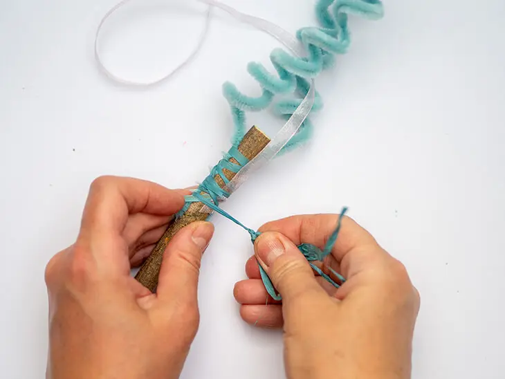 Jemand befestigt mit Naturbast von HEYDA Chenilledraht-Spiralen von KNORR prandell an einem Stock. Foto: Johanna Rundel