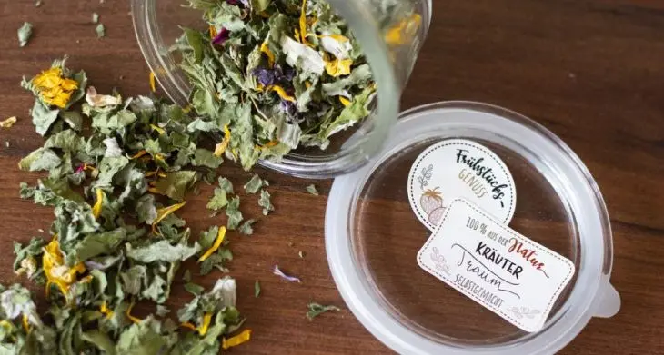 Selbstgemachter Kräutertee verteilt sich lose aus einem Marmeladenglas auf einem Holztisch