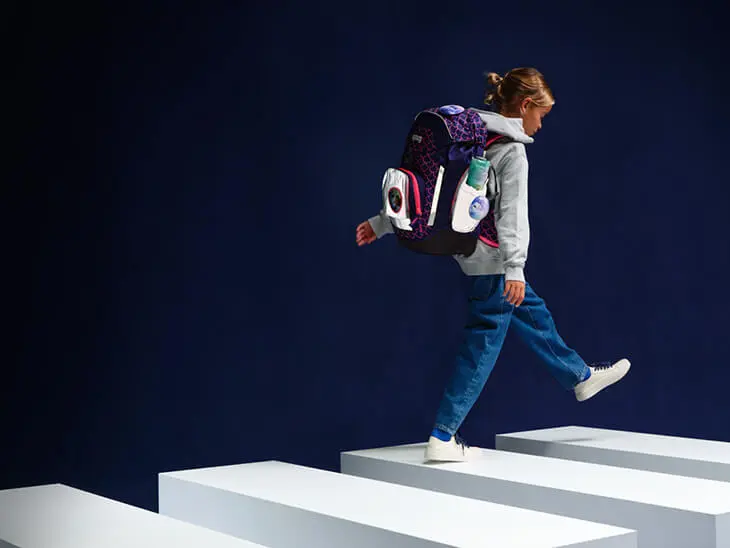 Ein Kind läuft mit einem reflektierenden Schulranzen von ergobag durch eine imaginäre Verkehrsszene.