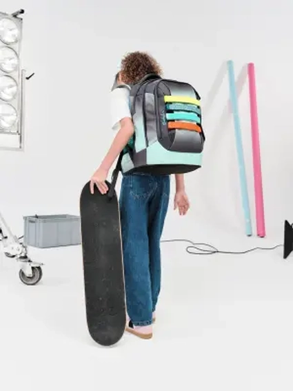 Zwei Jugendliche stehen Rücken an Rücken mit Schulrucksäcken von satch und blicken in die Kamera.