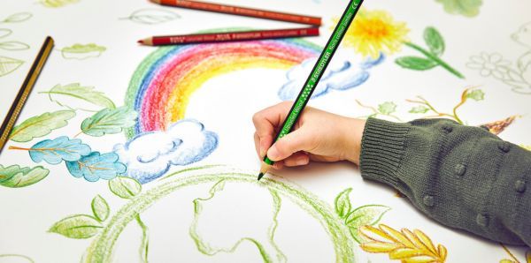 Eine Kinderhand malt mit Buntstiften ein Bild mit Regenbogen, Wolken, Blättern und der Erde.