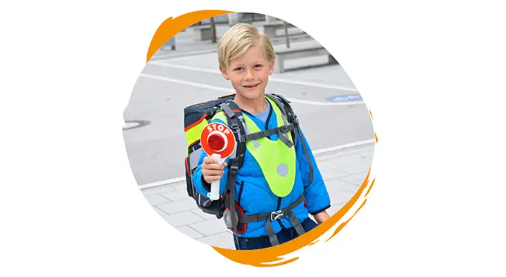 Ein Junge mit einem Schulranzen von Step by Step auf dem Rücken trägt eine Warnweste und hält eine Polizeikelle in die Kamera.