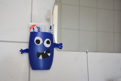 Aus einer leeren blauen Shampooflasche wurde ein Monster gebastelt, das als Aufbewahrungsbox dient. Es ist im Badezimmer an die Wand neben einen Spiegel geklebt und es stecken Zahnpasta und Zahnbürste drin.