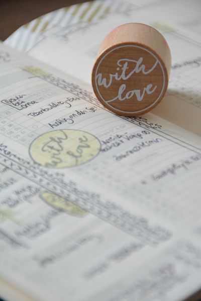 Nahaufnahme einer Kalenderseite mit vielen Notizen, darauf liegt ein Stempel mit dem Text "with love", welcher auch auf die Seite gestempelt wurde.