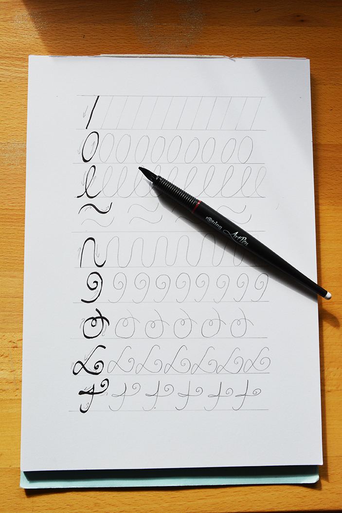 Geletterte Schwungübungen auf einem weißen Blatt Papier. Darauf liegt ein schwarzer Stift. 