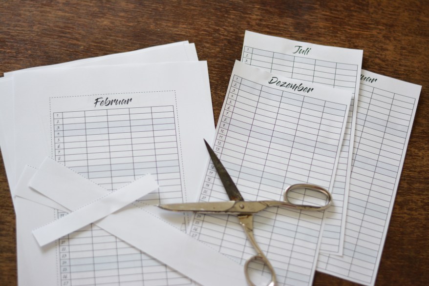 Kalenderblätter für verschiedene Monate mit Schere auf Holztisch.