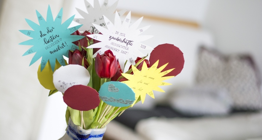 Gebastelte Papierblumen mit bunten Botschaften als Blumenstrauß zusammengebunden
