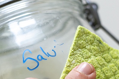 Nahaufnahme eines Weckglases, welches beschriftet wurde und der Schriftzug gerade mit einem Tuch weggewischt wird.