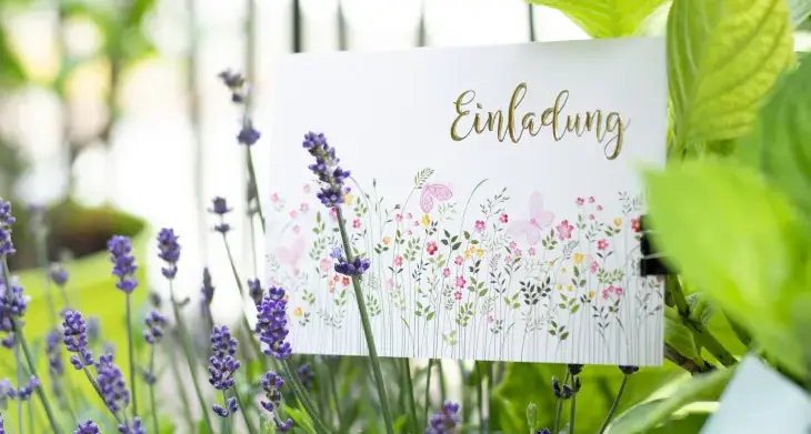 Eine Karte mit Blumenmuster und dem Wort "Einladung" steckt in einem Topf mit Lavendel.