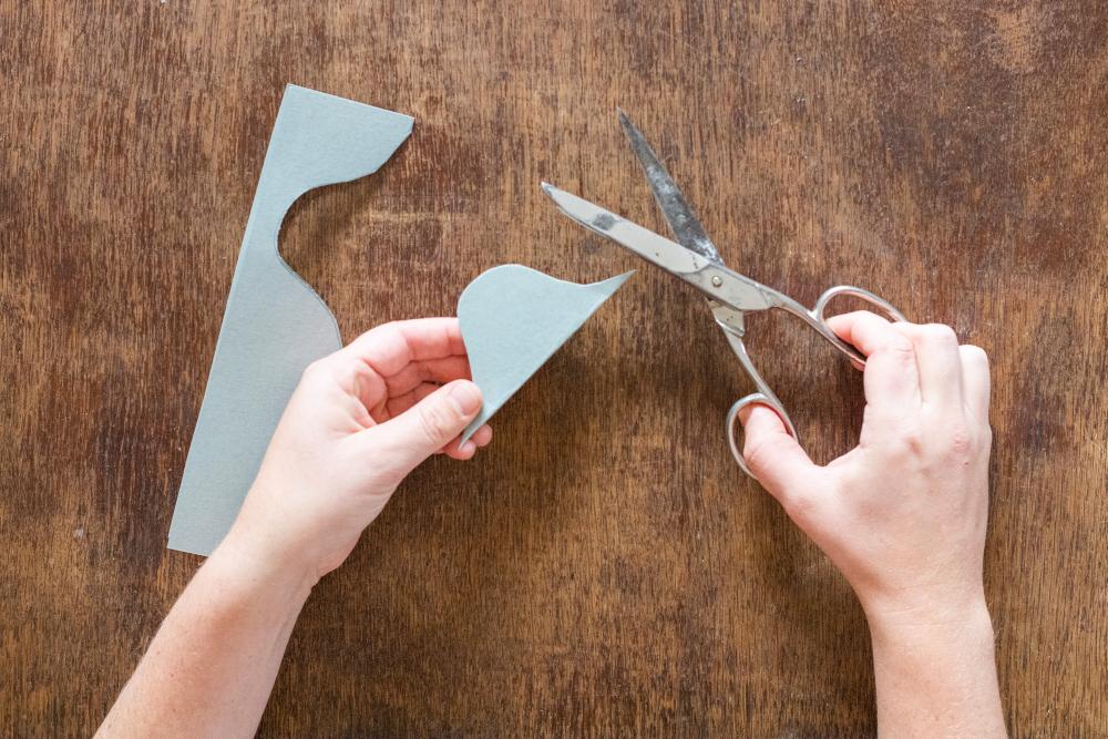 Eine Hand hält die ausgeschnittene Schablone, die andere Hand die Schere. 