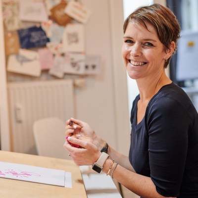 Diana Meier-Soriat vor ihrem Skizzentisch und lächelt in die Kamera.