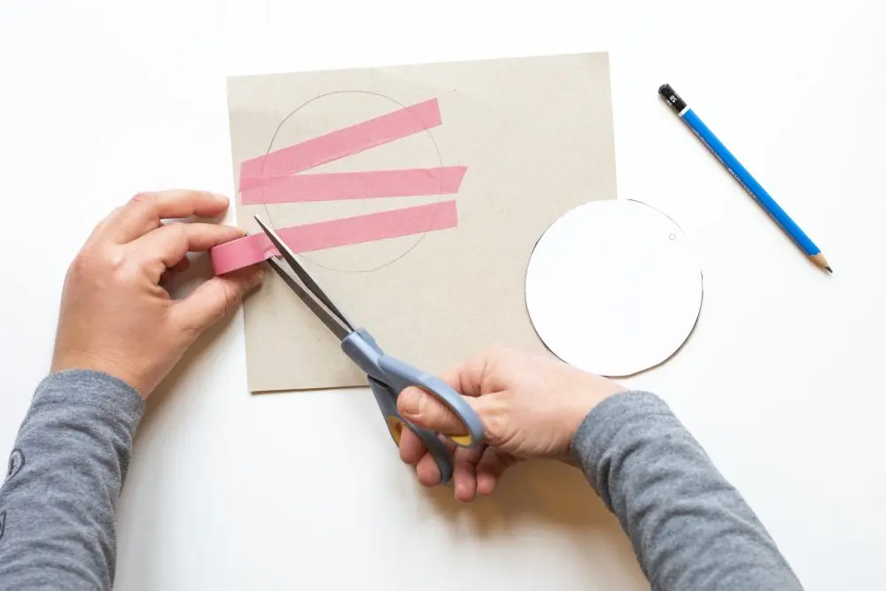 Jemand klebt mehrere Streifen Maskingtape über eine auf Papier gezeichnete, runde Geschenkanhängerform