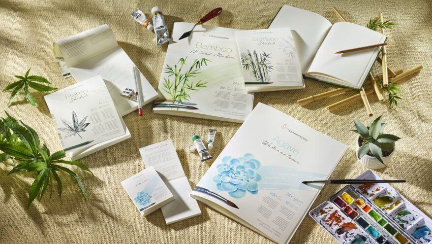 Verschiedene Malblöcke (Bamboo, Hanf, Agave) aus der Serie Natural Line von Hahnemühle liegen auf einem Stück Jutetuch, daneben liegen Pinsel und Aquarellkästen.