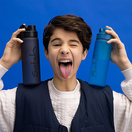 Vor einem blauen Hintergrund steht ein Jugendlicher und hält zwei blaue Trinkflaschen von satch auf seinen Schultern fest. Dabei zwinkert er in die Kamera und streckt die Zunge heraus.