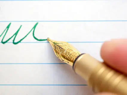 Ein Close-Up der Spitze eines goldenen Füllers von Kaweco, mit dem gerade eine Unterschrift in grüner Tinte auf ein liniertes Blatt geschrieben wird. Foto: Johanna Rundel 