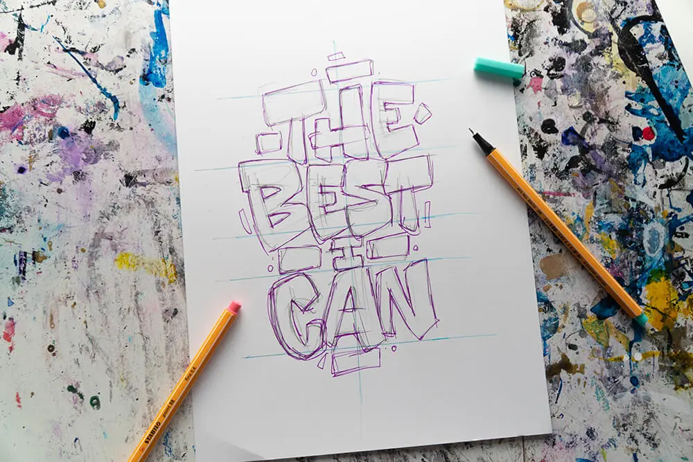 Auf einem weißen DIN A4 Blatt sind lila Buchstaben für ein Lettering vorgezeichnet. Daneben liegt ein Fineliner von Stabilo.