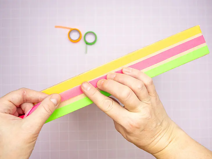 Jemand umklebt mit neonfarbigem Washitape von HEYDA den Rand des Deckels einer Pappschachtel von KNORR prandell. Foto: Johanna Rundel