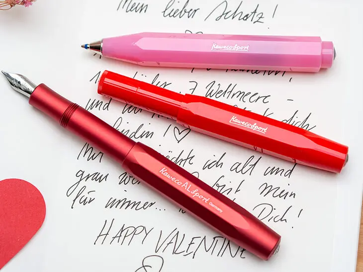 Ein pinker Kugelschreiber und zwei rote Füller von Kaweco liegen auf einer handgeschriebenen Karte zum Valentinstag. Foto: Johanna Rundel