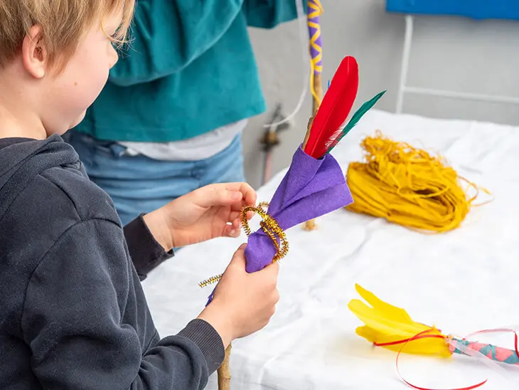 Zwei Grundschulkinder stehen an einem Tisch mit Bastelmaterialien von HEYDA und KNORR prandell und gestalten bunte Zauberstäbe aus Stöcken. Foto: Johanna Rundel