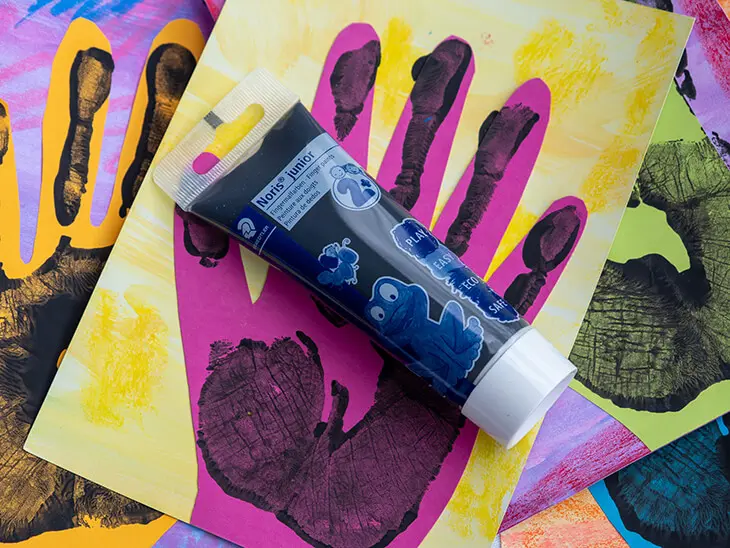 Eine schwarze Tube Fingerfarbe von STAEDTLER liegt auf einem Bild mit einem Handabdruck. Foto: Johanna Rundel