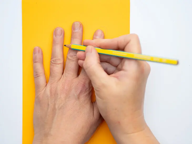 Jemand umfährt seine Hand mit einem Bleistift von STAEDTLER auf einem gelben Tonpapier. Foto: Johanna Rundel