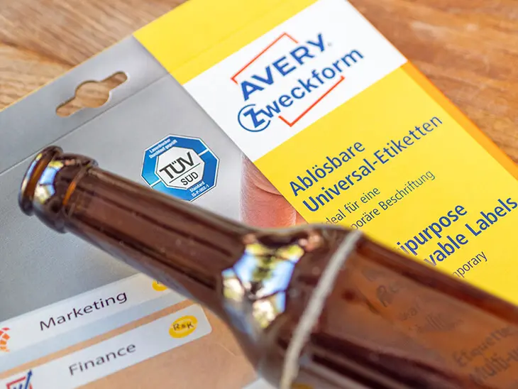 Auf einer Packung ablösbarer Universaletiketten von Avery Zweckform liegt eine braune Glasflasche. Foto: Johanna Rundel