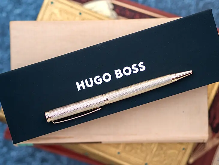 Goldener Kugelschreiber von HUGO BOSS liegt auf Bücherstapel. Foto: Johanna Rundel