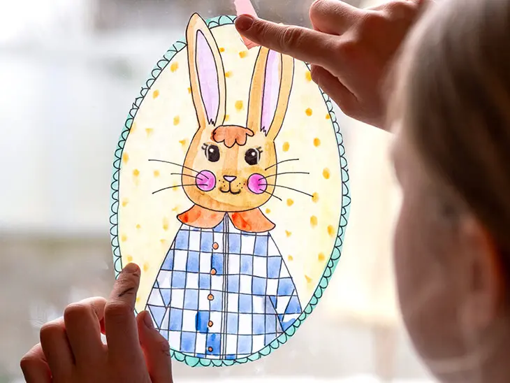 Ein Kind klebt ein buntes Osterhasen-Ausmalbild mit Tape ans Fenster. Foto: Johanna Rundel