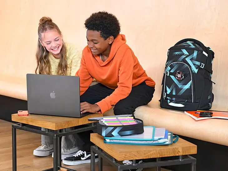 Zwei Teenager sitzen neben einem coocazoo Schulrucksack vor einem Laptop.