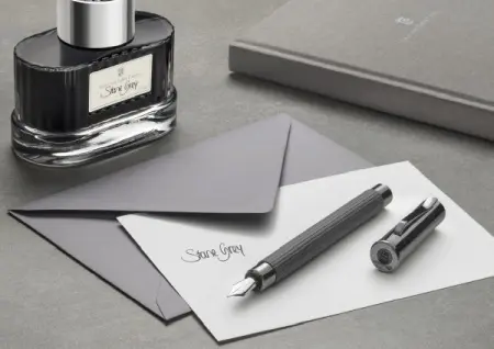 Der Füllhalter Tamitio von Graf von Faber-Castell in der Farbe Stone Grey liegt in einem grauen Setting auf einer Karte mit Briefumschlag