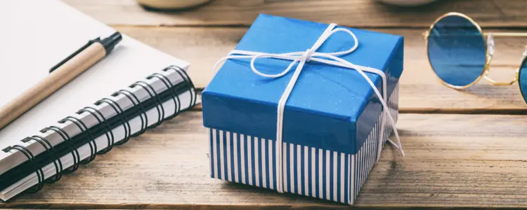 Auf einem Tisch liegt ein Geschenk, daneben ein Block und Sonnenbrille