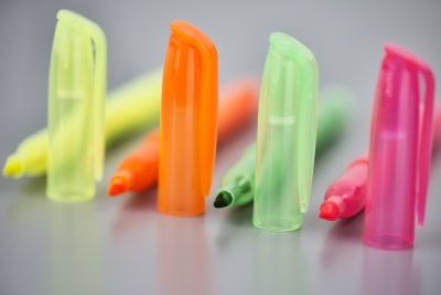 Nahaufnahme von 4 farblichen Markern, deren Kappen aufgestellt auf dem Tisch stehen.