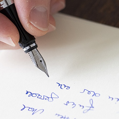 Nahaufnahme einer Füllfeder der Marke Online beim Schreiben mit blauer Tinte auf cremefarbenem Papier.