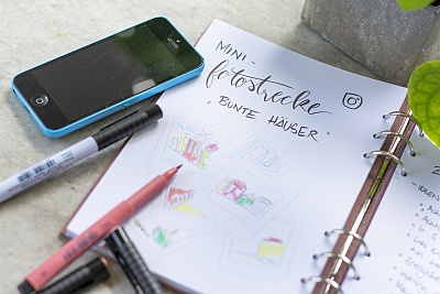 Skizzenbuch mit Notizen und Zeichnungen, umgeben von Stiften und Smartphone.