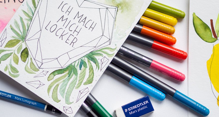 Mit einem Spruch gestaltete Karte, bunte Stifte und Radiergummi auf einem Tisch