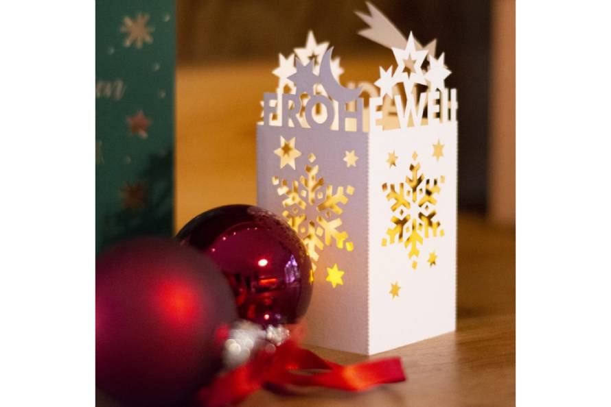 Papier-Windlicht mit ausgestanzten Schneeflocken und Schriftzug Frohe Weihnachten.